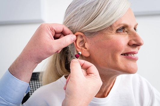 Seniorin bekommt ein modernes Hörgerät angepasst und lächelt zufrieden beim Hörtest.